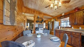 Un interno in legno con un tavolo da pranzo imbandito per quattro persone, una cucina con pensili in legno e una ventola a soffitto.