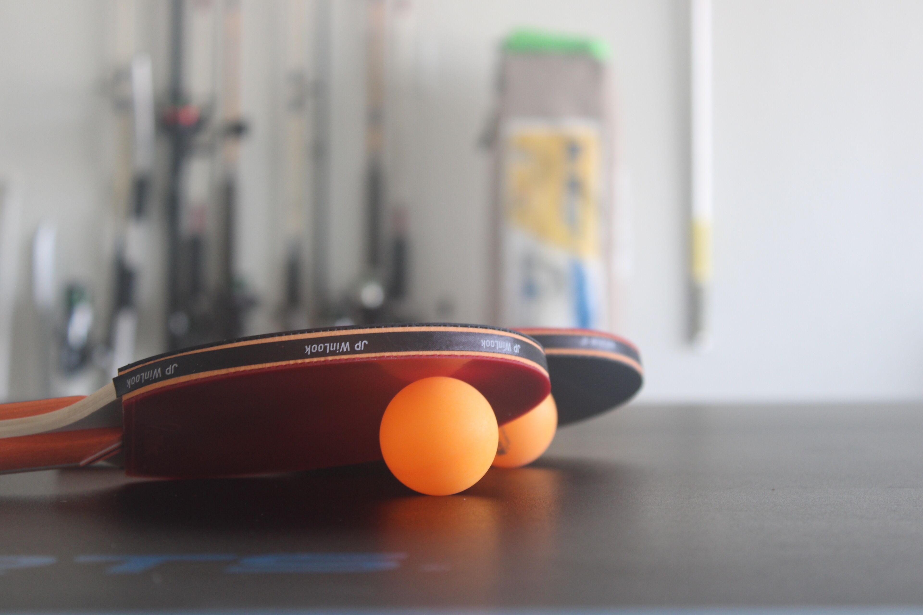 Detailaufnahme von zwei Tischtennisbällen auf einem Tisch, im Hintergrund verschwommen Sportgeräte.