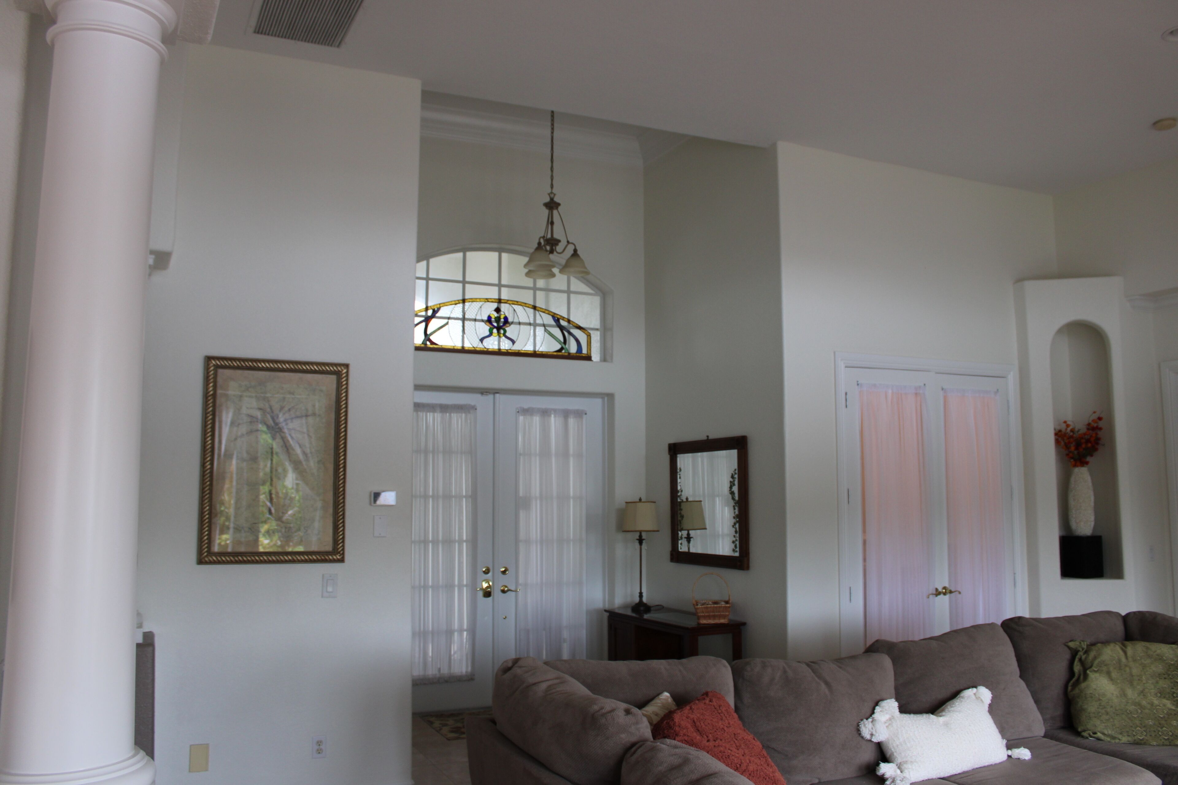 A living room with a large window, a sofa, a lamp, and a framed picture on the wall.