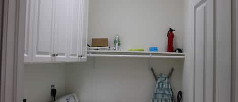 A laundry room with a washing machine, a dryer, a shelf with cleaning supplies, and a fire extinguisher.