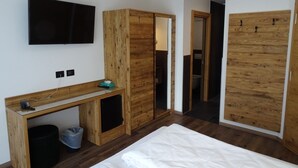 Une chambre moderne avec un bureau en bois, un téléviseur fixé au mur et une grande armoire.
