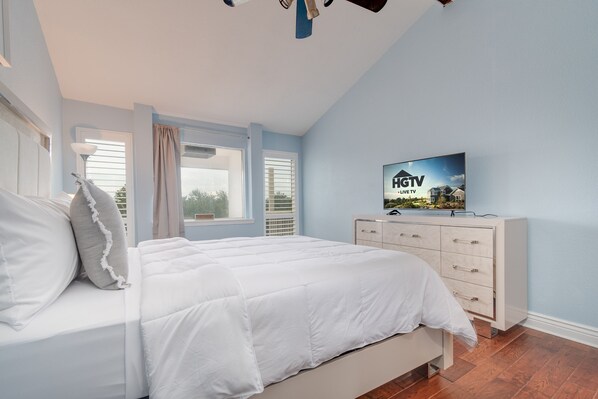 Ein Schlafzimmer mit Bett, Schminktisch, Fernseher und einem Fenster mit Jalousien.