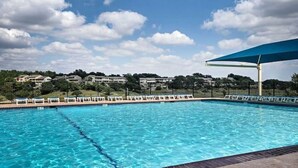 Ein Schwimmbecken mit klarem, blauem Wasser, umgeben von Liegestühlen und einem großen, blauen Sonnenschirm.