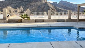 Piscina con vista a la montaña, terraza de concreto y cerca blanca.