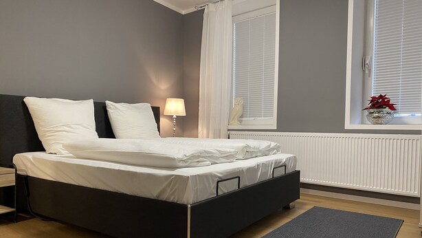 Una camera da letto moderna con un letto, un comodino, una lampada, una finestra con persiane e un termosifone.