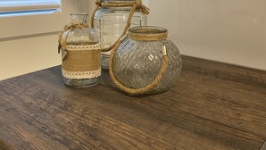 Un tavolo di legno con tre barattoli di vetro legati con lo spago, posizionato su un ripiano della cucina vicino a una finestra con persiane.