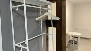 Un armadio in metallo bianco con coperchio a rete, un'asta appendiabiti e dei ganci.