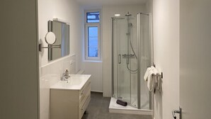 Un bagno moderno con cabina doccia in vetro, lavabo con specchio e finestra che permette l'ingresso di luce naturale.