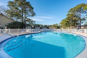 Una piscina azul cristalina rodeada por una valla blanca, con sillones de descanso y un edificio al fondo.