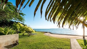 A well-maintained garden with a pathway leading to a beach, palm trees, and a clear view of the ocean. - RCG Suites Pattaya (Pattaya)