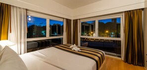 A hotel room with a large bed, two windows, and a view of the city at night. - RCG Suites Pattaya (Pattaya)