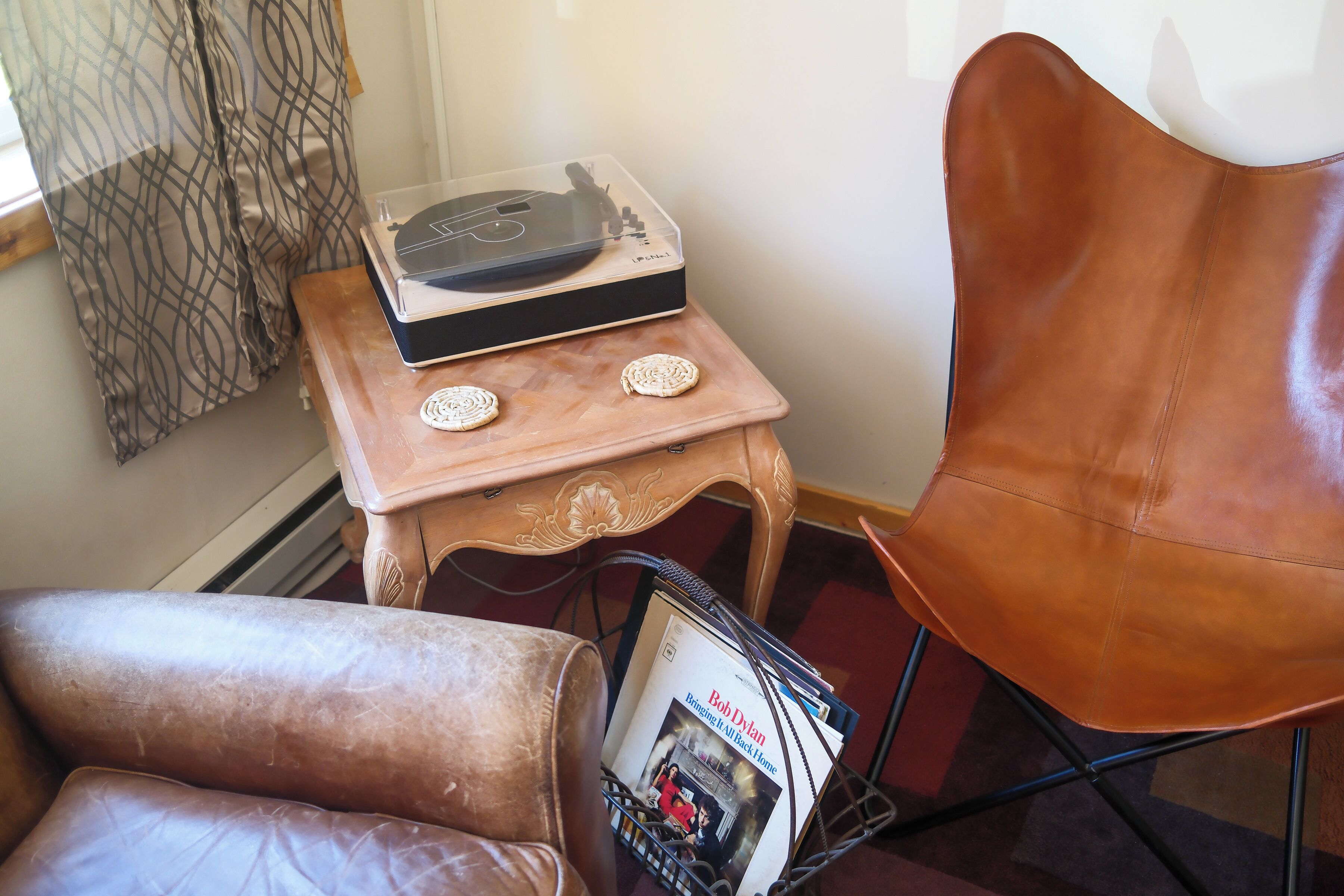 A room with a brown leather chair, a small wooden table with a record player, and a magazine rack.