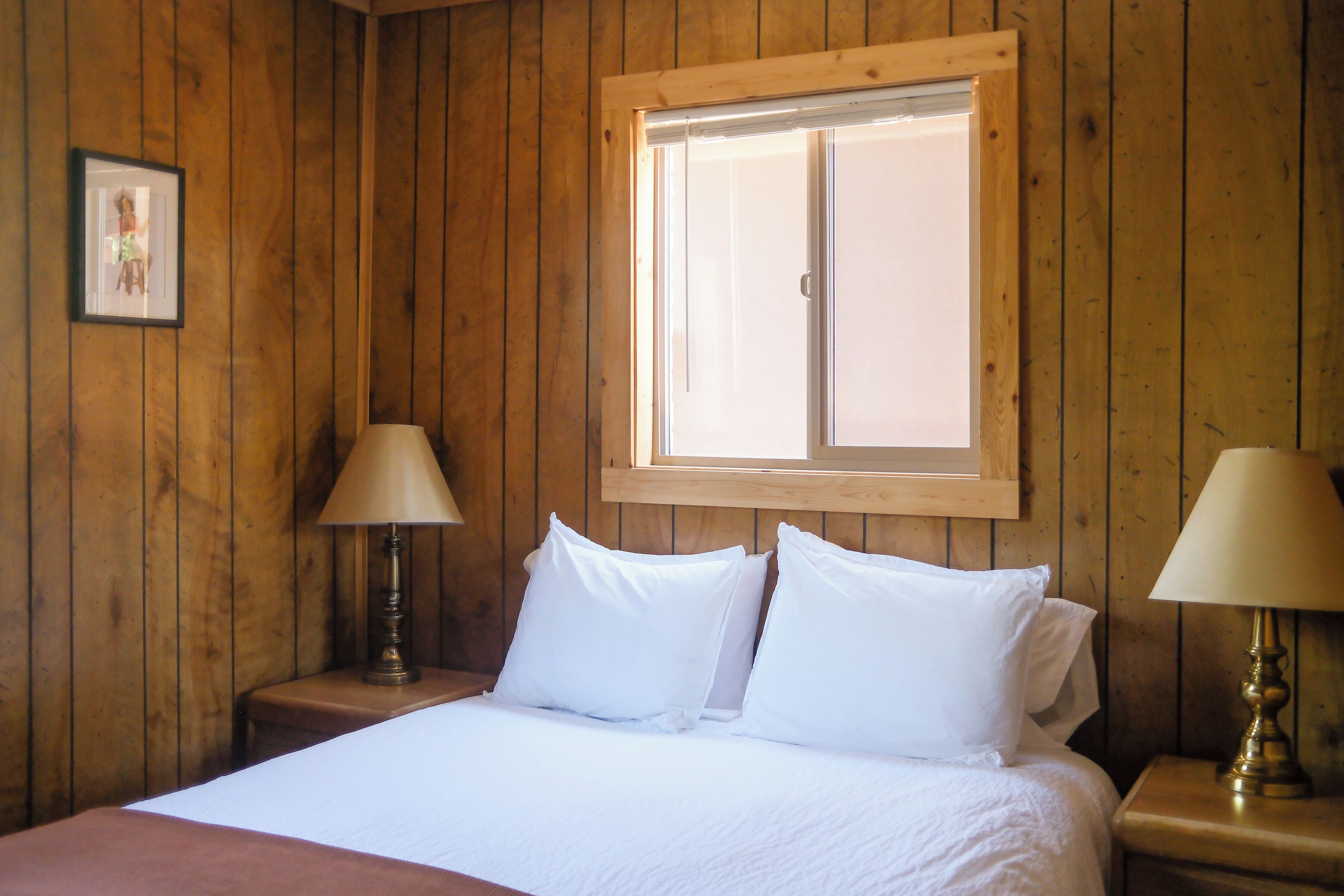 Una habitación con paneles de madera, una cama, dos lámparas de noche y un ventanal.