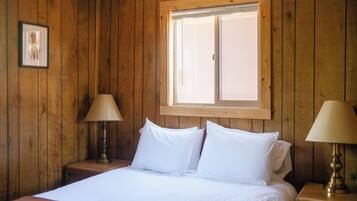 Una habitación con paneles de madera, una cama, dos lámparas de noche y un ventanal.