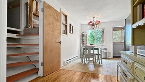 A spacious room with a wooden floor, a dining area with a table and chairs, a chandelier, and a bookshelf. - Rocky Mountain Inn (Paonia)