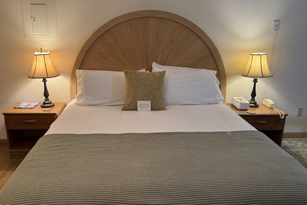 A neatly made bed with a large wooden headboard, two bedside tables with lamps, and a bedside phone.