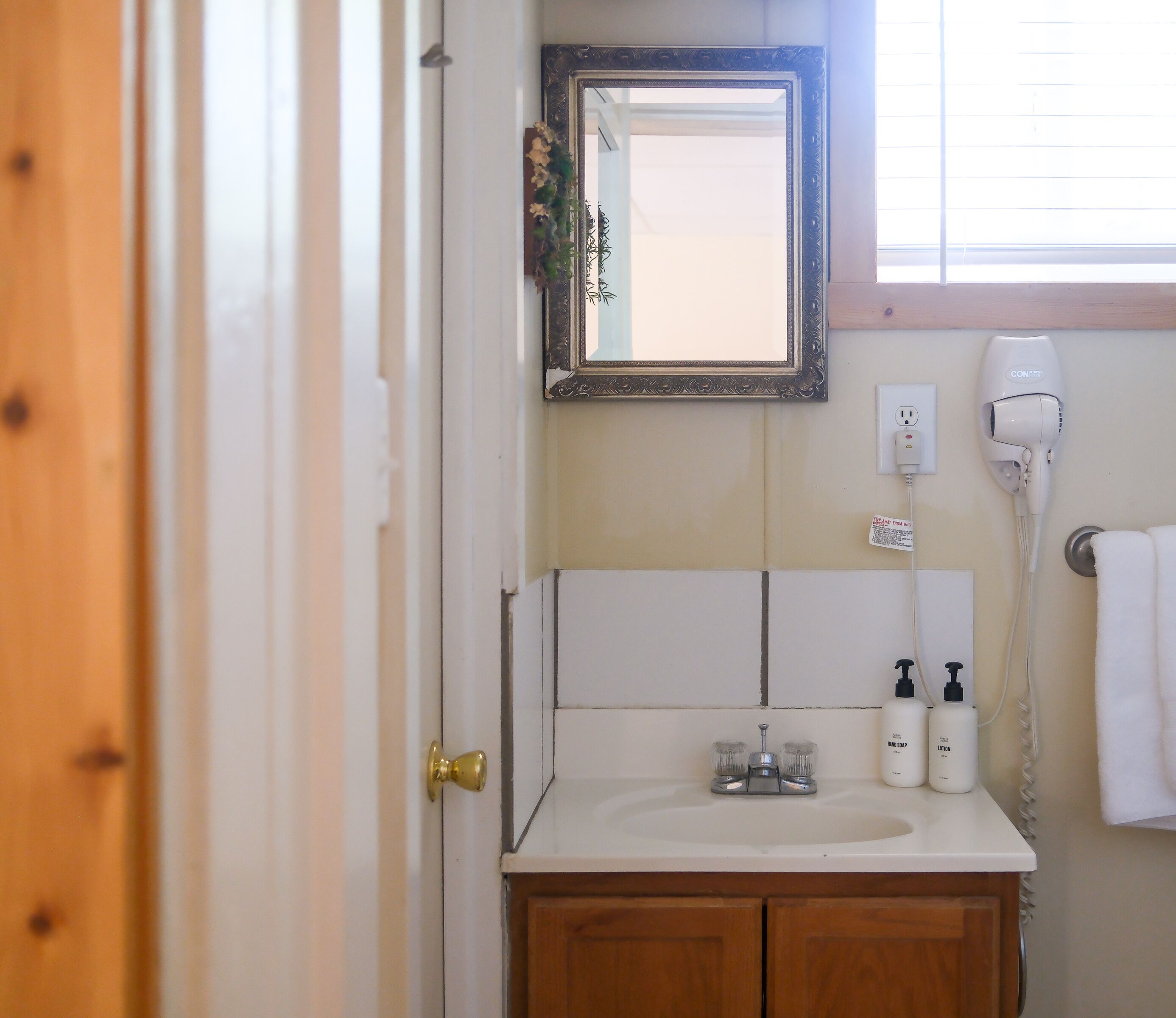 A bathroom with a sink, mirror, hairdryer, and toiletries.