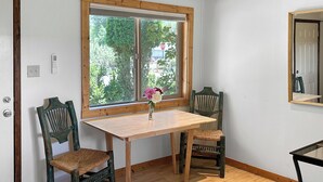 A room with a wooden table, two chairs, a window with blinds, a wall-mounted light fixture, and a door. - Rocky Mountain Inn (Paonia)