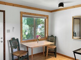 Una habitación con una mesa de madera, dos sillas, un ventanal con persianas, una lámpara de pared y una puerta.