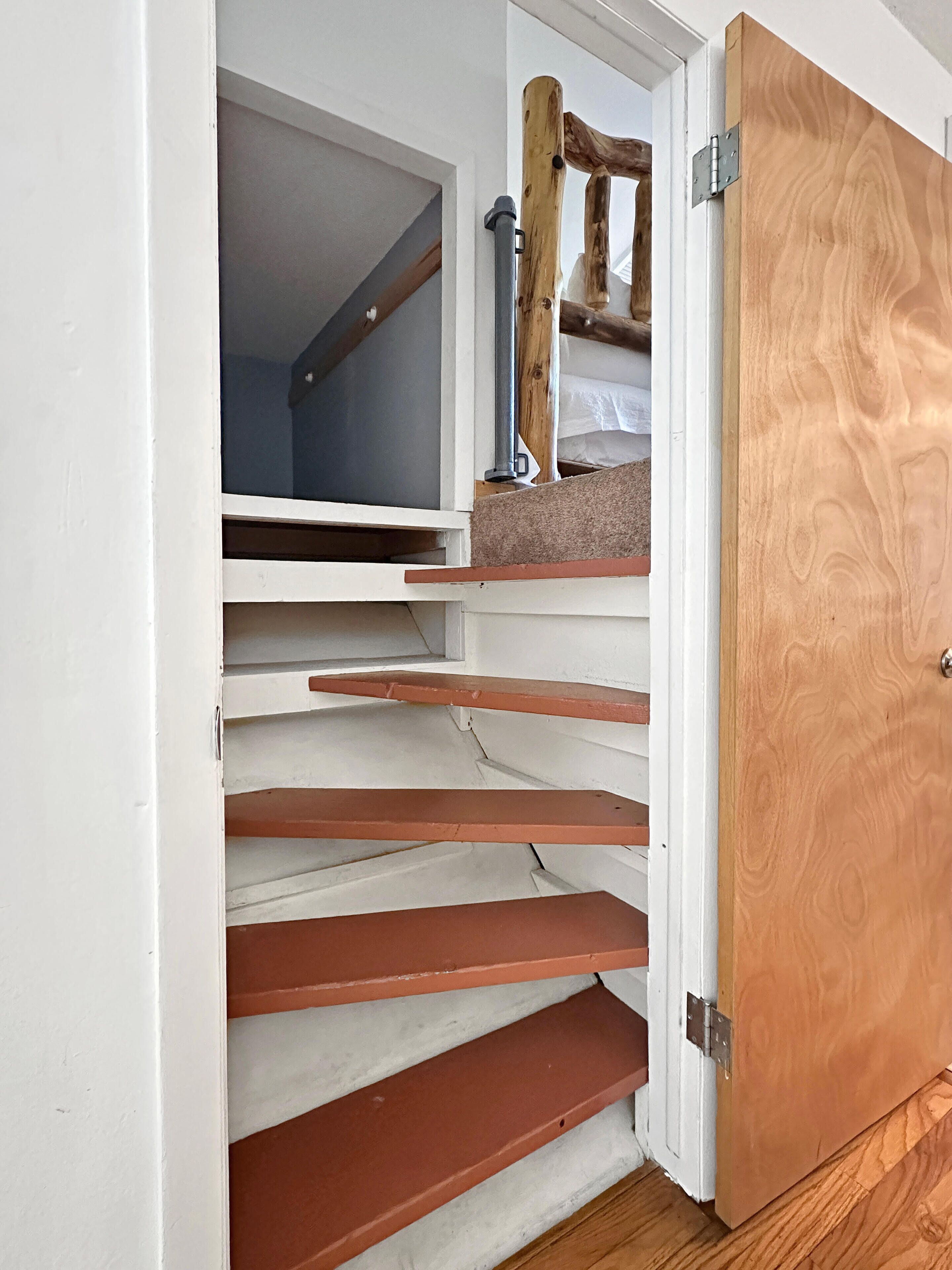 Una porta di legno con un chiavistello metallico, un muro bianco e una scala con gradini marroni.
