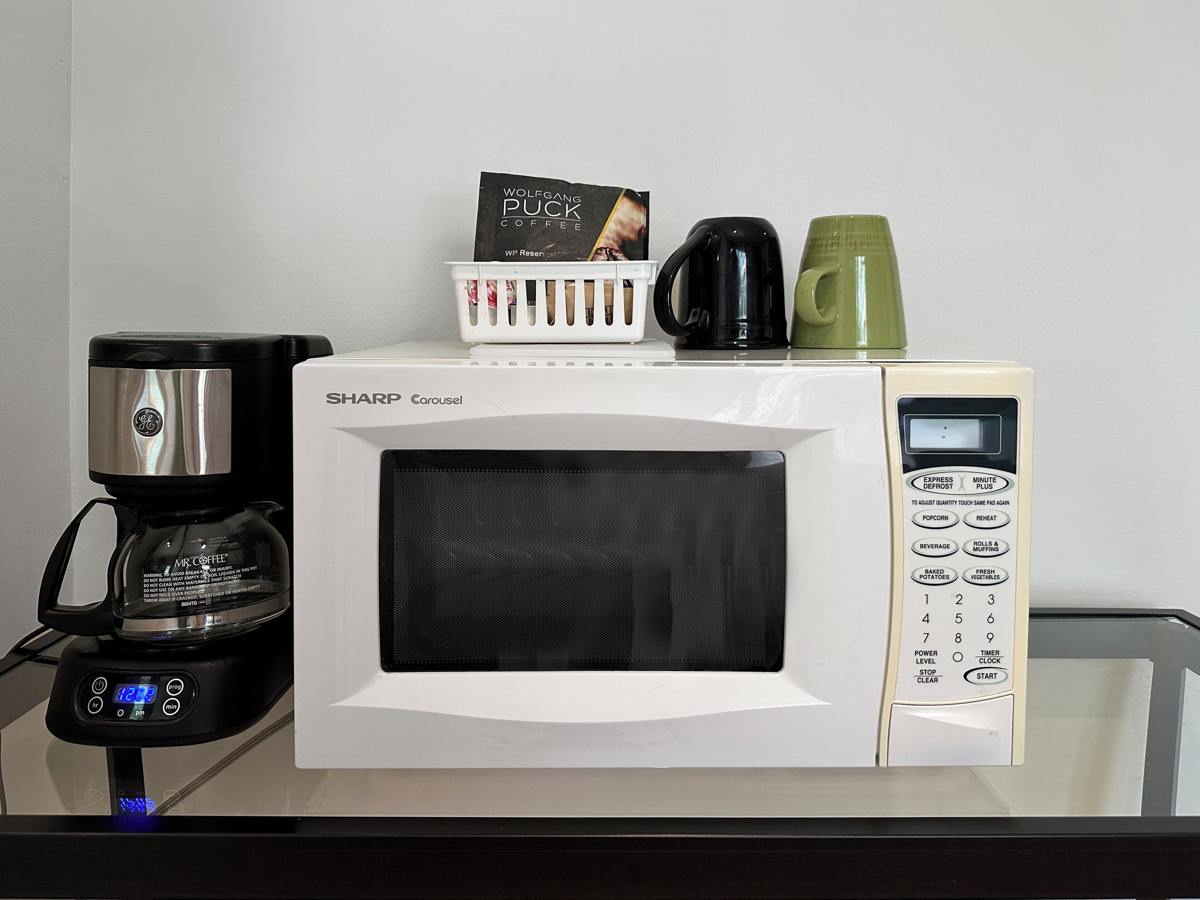 Un horno microondas con una cafetera y una jarra de café encima.