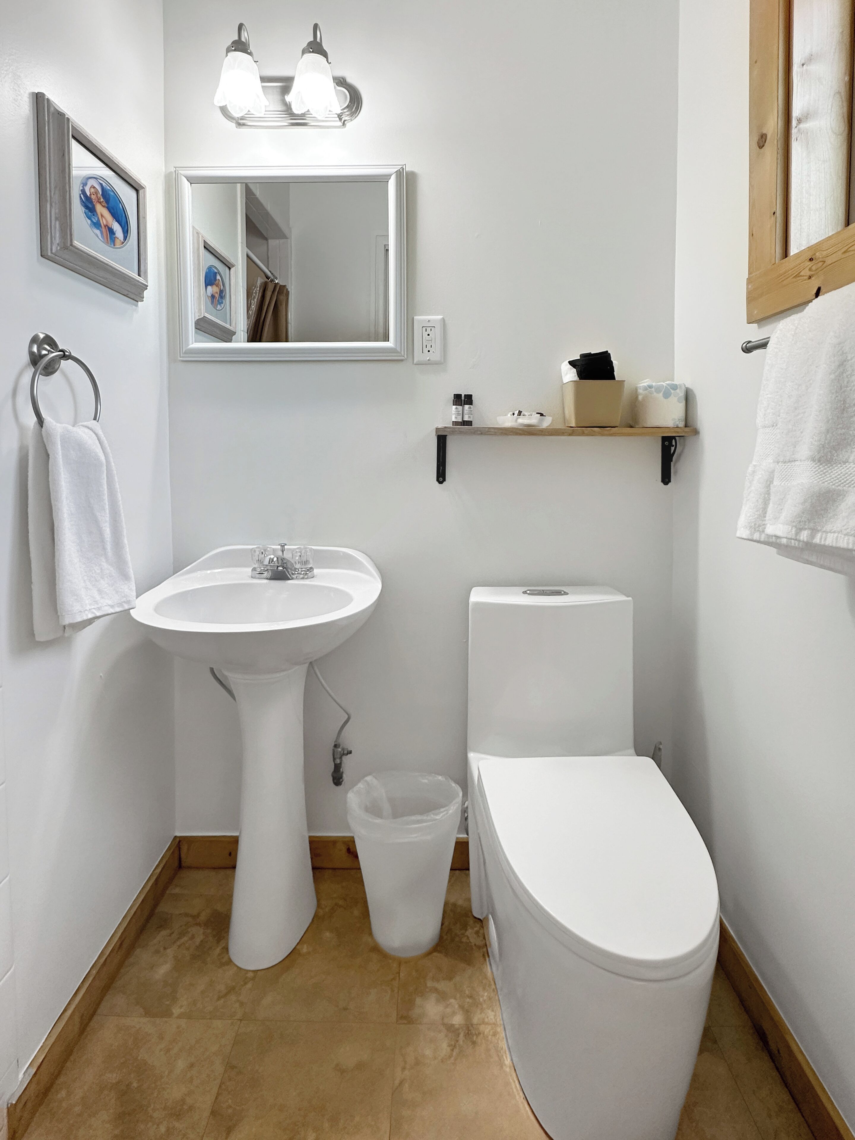 Un baño con lavamanos blanco, espejo, inodoro y un pequeño cubo de basura.