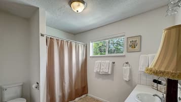 A bathroom with a toilet, shower curtain, sink, and window.