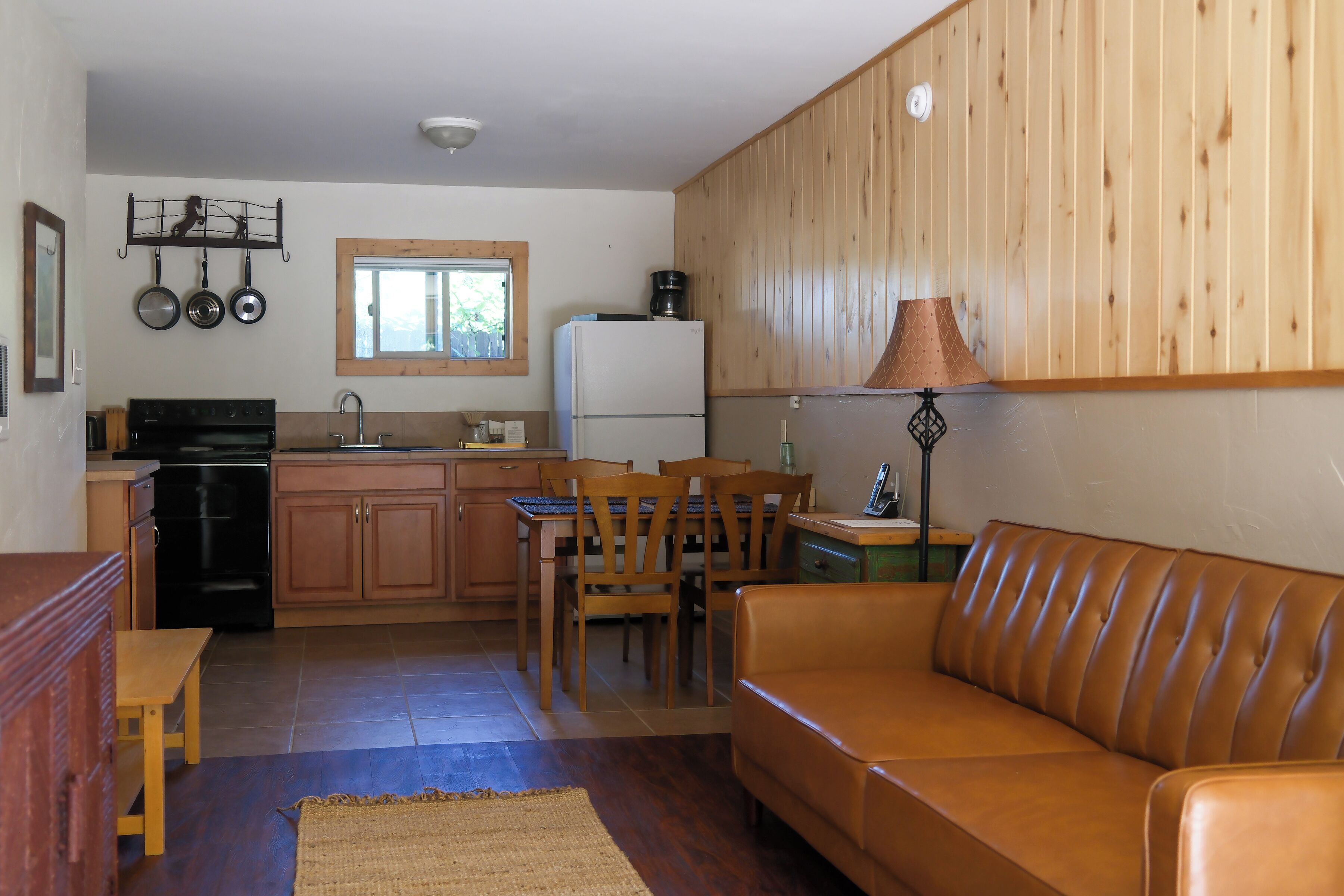 A compact kitchen with wooden cabinets, a dining area with a table and chairs, and a brown leather sofa.