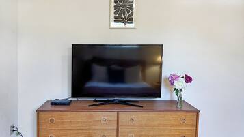 Un mueble bajo de madera para televisor con un televisor de pantalla plana, una obra de arte enmarcada encima y un florero con flores a la derecha.