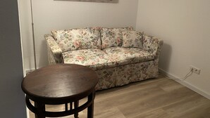 Una habitación de esquina con un sofá estampado con motivos florales, una mesa de madera y un aplique de pared.