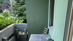 Un pequeño patio al aire libre con una mesa, dos sillas, un cesto de basura y una pared verde.