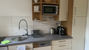 Una cocina compacta con un lavamanos, microondas, hervidor y escurreplatos.
