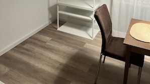 Una habitación con una estantería blanca, una silla marrón, una mesa de madera y una lámpara colgante.
