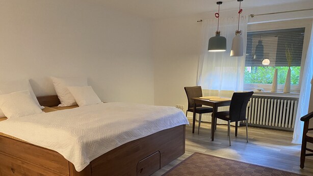 Un dormitorio con cama de madera, una mesa de comedor con sillas y vistas a la vegetación a través de la ventana.