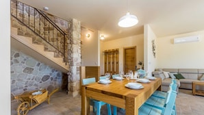 A dining area with a wooden table set for four, a stone staircase, and a living room with a sofa. - Rustic Villa BELLAMARE with pool (Linardići)