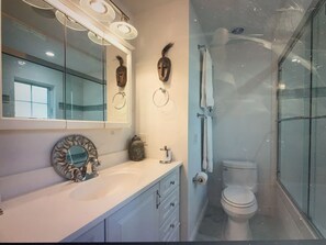 Une salle de bain comprenant un meuble-lavabo, un miroir, des toilettes et un espace douche.