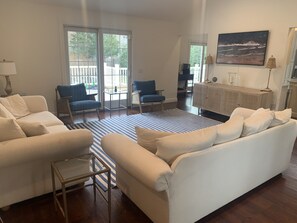 A spacious living room with a white sofa, blue armchairs, a striped rug, and a large window with a view of a deck.