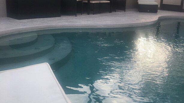 A swimming pool with a curved edge, surrounded by a tiled deck. There are lounge chairs and a small table with chairs. - 3 Bedroom/2 Bathroom Home with Enclosed Porch (Sleeps 5-6) (Davenport)