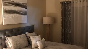 A neatly made bed with a patterned bedspread and pillows, a headboard, a wall-mounted lamp, and a curtain with a patterned design. - 3 Bedroom/2 Bathroom Home with Enclosed Porch (Sleeps 5-6) (Davenport)