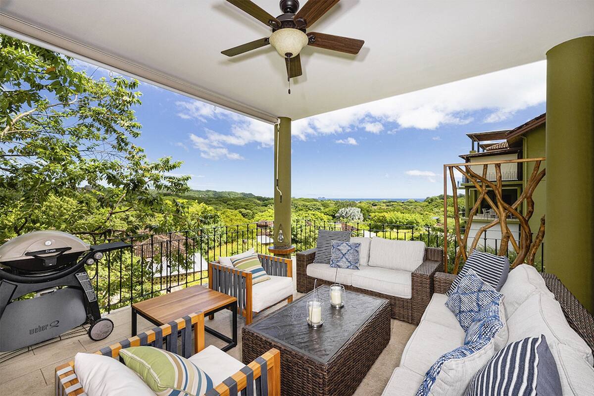 A balcony with wicker furniture, a ceiling fan, and a view of a lush landscape.