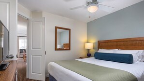 Hotellihuone, jossa on sänky, puinen pääty, yöpöytä lampun kanssa, peili ja kattotuuletin.