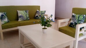 A green sofa with matching cushions, a white coffee table, and a white chair with a geometric backrest. - White House Mtwapa (Mtwapa)