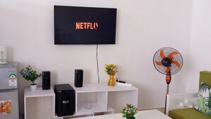 A living room with a TV displaying the Netflix logo, a white console table with speakers, a fan, and decorative items. - White House Mtwapa (Mtwapa)