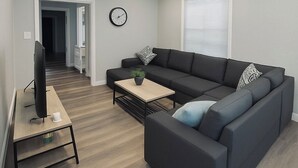 Un soggiorno moderno con un divano nero, un tavolino, una TV e una ventola a soffitto.