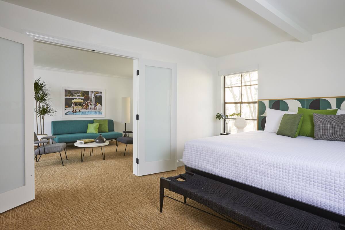 Una habitación de hotel moderna con una cama grande, un sofá, una mesa de centro y vistas a una zona de piscina.
