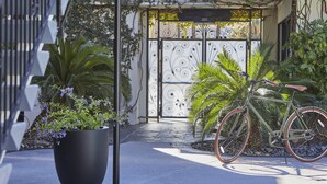 Ein Fahrrad vor einem Gebäude mit schmiedeeisernem Tor, umgeben von üppiger Vegetation und einem Blumentopf.