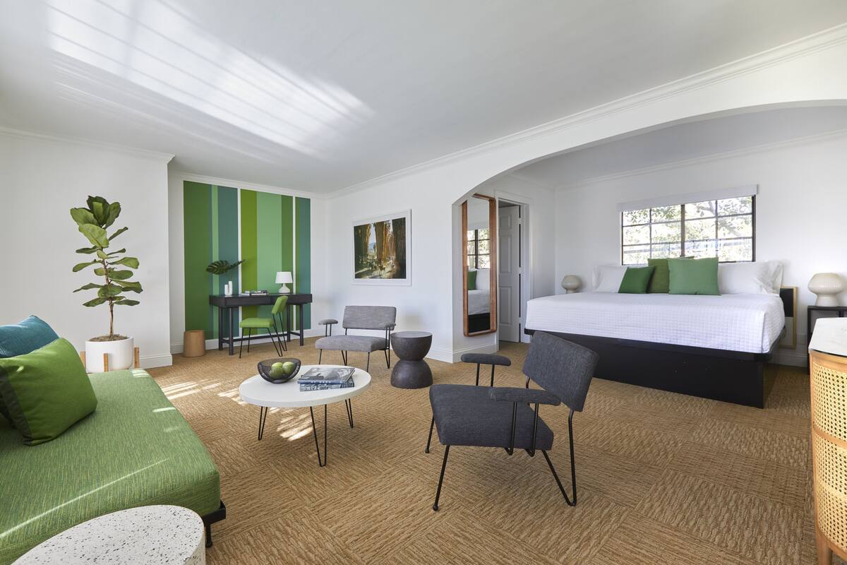 Una habitación de hotel moderna con una cama, un sofá verde y un área de comedor con sillas y una mesa.