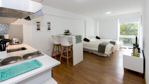 Una cocina moderna con un lavamanos, estufa y taburetes de bar. Hay un pequeño comedor con una mesa y sillas. La habitación tiene un ventanal y una cama con vistas.