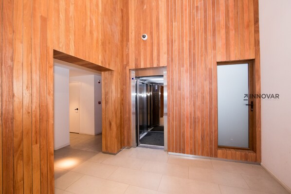A modern hallway with wooden paneling, a glass elevator, and a door with a nameplate.