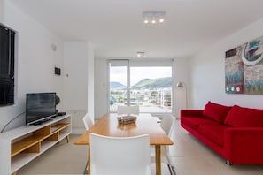 Ein modernes Wohnzimmer mit Essbereich, einem roten Sofa und einem Fernseher auf einem weißen Schrank.